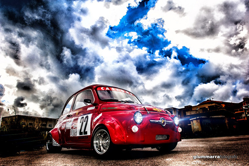 Una Cinquecento da corsa e sullo sfondo un paesaggio comisano